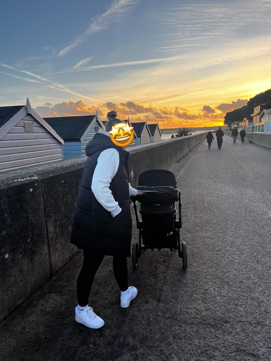 Bugaboo Fox 5 in bassinet mode being pushed along a seafront path beside beach huts at sunset